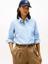 Camisa de corte regular confeccionada en popelín de algodón elástico con diseño de rayas verticales finas en color celeste y blanco. Presenta cuello clásico, cierre frontal con botones y logo de la marca bordado en el pecho.