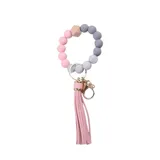 Llavero con pulsera elástica de cuentas redondas de silicona en tonos rosa, gris y blanco, con un cubo de madera natural y una borla rosa.