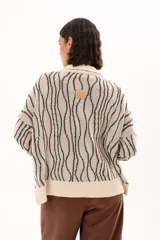 Buzo de tejido de punto con diseño de rayas verticales onduladas en tonos verde y marrón sobre base color crudo. Presenta cuello tipo polo con cierre frontal de botones y mangas largas con puños acanalados.