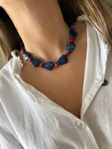 Collar corto con cuentas irregulares de resina azul con efecto marmolado, intercaladas con cuentas pequeñas de coral rojo.