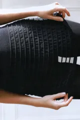 Top negro con cuello halter ajustable mediante lazo. La parte superior es opaca y ajustada, mientras que la parte inferior presenta un tejido semitransparente con franjas horizontales en relieve.