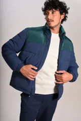 Campera puffer con diseño bicolor, cuerpo en azul marino y canesú superior en verde oscuro. Presenta cuello alto, cierre frontal completo y puños elásticos.