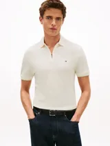 Chomba de piqué de algodón mercerizado color blanco hueso, con cuello de chomba y cartera con cremallera. Presenta un logo Tommy Hilfiger bordado en el pecho.