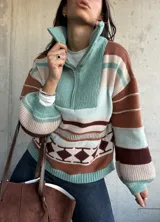 Sweater de tejido de punto con diseño a rayas horizontales y patrón geométrico en tonos verde, marrón y beige. Presenta cuello alto con cierre frontal, mangas largas abullonadas con puños ajustados y corte holgado.