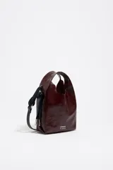 Mini bolso de hombro Bimba Y Lola modelo Paper, confeccionado en piel vacuna color marrón con acabado acharolado arrugado. Cuenta con asas de mano integradas, correa de hombro ajustable y detalles metálicos con el logo de la marca impreso en la parte inferior.
