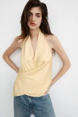 Top de tejido satinado con cuello halter y escote en pico cruzado. Presenta un diseño de espalda descubierta y bajo asimétrico con cierre lateral.