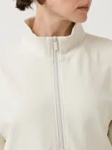 Buzo color beige con cierre frontal parcial y cuello alto. Presenta un bolsillo tipo canguro con diseño tejido a rayas horizontales en tonos marrón, beige y blanco.