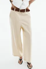 Pantalón culotte de tiro alto color beige, confeccionado con lino. Presenta pernera ancha y corta, bolsillos delanteros y falsos bolsillos de vivo en la espalda. Incluye un cinturón marrón con hebilla metálica redonda y cierre frontal con cremallera, botón interior y gancho.