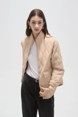 Campera acolchada de poliamida en color beige, con diseño de costuras en rombos, cuello alto, cierre frontal y bolsillos delanteros con solapa.