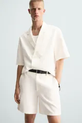 Bermuda de algodón color blanco, de corte relajado, con cintura elástica, bolsillos frontales y bolsillos traseros de plastrón. Cierre frontal con cremallera y botón.