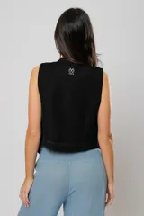 Chaleco negro con escote en V, sin mangas y cierre frontal con botones. Presenta pespuntes en color crudo en la parte delantera y logo bordado en la espalda.