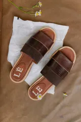 Sandalias tipo chinelas de cuero marrón con diseño de doble banda, una de cuero texturizado tipo cocodrilo y otra de gamuza. Presentan plantilla de cuero con logo grabado y suela plana.