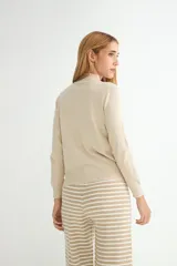 Polera de punto color beige, con cuello alto y mangas largas, de diseño básico y ajuste clásico.