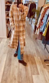 Tapado largo de paño liviano con diseño de cuadros en tonos marrones. Presenta solapas clásicas, bolsillos laterales con detalles en cuero y tajos profundos en los costados.