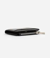 Billetera femenina Satinato tipo sobre, confeccionada en PU color negro con estructura firme, cierre con botón a presión, bolsillo externo con cierre metálico, compartimentos internos y placa metálica frontal con logo.