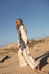 Pantalón de lino de corte ancho y tiro medio, color natural, con detalles de bandas laterales y cintura en estampado rayado azul y marrón.