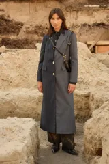 Tapado largo de sastrería con diseño bicolor y asimétrico. Una mitad presenta un tejido negro con rayas diplomáticas, mientras que la otra mitad es de un tejido a cuadros en tonos tierra. Cuenta con botones de nácar, bolsillos con tapa y abertura trasera.