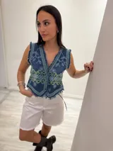Chaleco corto en denim azul con detalle desflecado y bordado artesanal en tonos celeste y dorado. Estilo boho chic con escote en V, ideal para combinar con prendas básicas y elevar tu look.