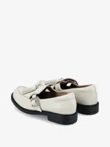 Zapato tipo guillermina o mary jane de cuero negro, con cierre de hebilla lateral, detalle de flecos en el empeine y tachas metálicas decorativas en el borde frontal.