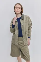Campera de gabardina verde militar, de corte holgado, con cuello camisero, cierre frontal de botones y bolsillos delanteros con solapa.