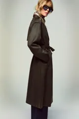 Abrigo largo color marrón oscuro con efecto ante, cuello solapa, manga larga con trabillas en los hombros y bolsillos delanteros de vivo. Presenta un bajo con abertura en la espalda y cierre frontal cruzado con botones, complementado con un cinturón a tono.