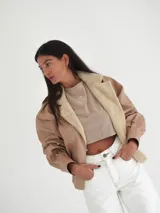 Campera oversize de cuero tostado con solapas y forro interno de corderito sintético azul marino, mangas anchas y detalles de costuras trenzadas.