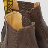 Botas Chelsea Dr. Martens modelo 2976, confeccionadas en cuero Crazy Horse color marrón con acabado envejecido. Presentan paneles elásticos laterales, suela de goma con costuras amarillas características y tirador trasero.