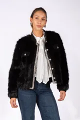 Chaqueta de piel sintética negra con corte recto, cuello redondo y cierre frontal con botones perlados. Presenta detalles de bordes con apliques de strass brillantes y bolsillos frontales con solapa.