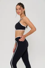 Conjunto deportivo compuesto por un top y calzas largas. El top es negro con bordes blancos y logo estampado en el frente. Las calzas son negras con cintura cruzada en V, detalles de líneas laterales blancas y logo estampado en la pierna.