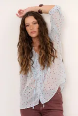 Blusa marrón semitransparente con estampado de lunares celestes, mangas largas abuchonadas, cuello en V con lazos y detalles de volados frontales.