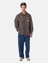 Camisa de manga larga Carhartt con estampado camuflado en tonos verdes y marrones. Presenta cuello clásico, cierre frontal con botones, un bolsillo en el pecho con etiqueta de la marca y puños abotonados.