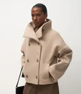 Saco femenino de estructura encorpada en color beige, con cuello alto, cierre frontal de abotonado traspasado y mangas largas de caída recta.