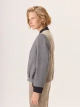 Chaqueta tipo bomber de lana con estampado de espiga en tonos grises. Presenta cuello, puños y ruedo en tejido elástico negro, cierre frontal dorado y bordado sutil en el pecho.