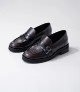 Mocasín de cuero vacuno negro con detalle de pieza de cuero con textura de cocodrilo y hebillas metálicas. Suela de caucho con plataforma.