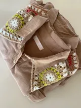 Camisa tostada de manga larga con cuello clásico decorado con apliques de crochet en tonos marrones, blancos y verdes, cierre frontal de botones y diseño holgado.