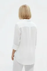 Camisa de algodón color beige, de corte holgado, con mangas tres cuartos, cuello camisero y cierre frontal de botones.