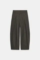 Pantalón balloon de tiro alto y diseño abuchonado, en color marrón oscuro con sutiles rayas verticales. Cuenta con pinzas y pliegues pronunciados en el delantero.