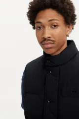 Chaleco puffer negro con cuello alto, cierre frontal de cremallera y botones a presión.