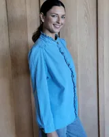 Camisa de jean azul con cuello alto con volados y volados en el frente.