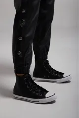 Pantalón negro de cuero sintético con bolsillos laterales y botones metálicos a presión en los laterales.