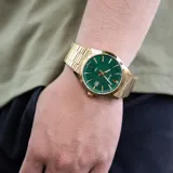 Reloj Casio dorado con esfera verde con diseño de tablero de ajedrez, agujas y marcadores dorados, indicador de fecha y pulsera de acero inoxidable dorada.