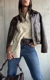 Camisa de color beige con diseño de broderie anglaise, cuello clásico, cierre frontal con botones y mangas largas.