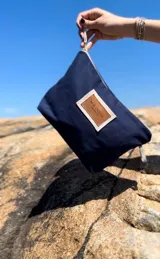 Nécessaire azul marino de lona con cierre superior y etiqueta frontal de cuero sintético marrón con el logo de la marca.