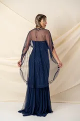 Vestido largo de fiesta color azul, confeccionado en tul bordado con diseño strapless. Incluye una capa tipo poncho de tul transparente con detalles bordados a juego, que cubre los hombros y cae hacia la espalda.