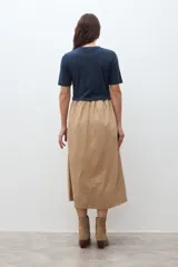 Vestido de dos piezas, con la parte superior tipo camiseta de manga corta y cuello redondo en color azul marino, y la parte inferior tipo falda midi de corte amplio y fruncido en color beige.