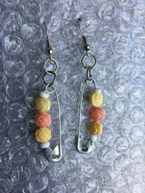 Par de caravanas colgantes hechas con imperdibles plateados, aros plateados y cuentas de fantasía con forma de rosa en color amarillo, naranja y blanco.