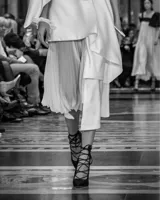 Falda asimétrica de tiro alto color blanco, confeccionada en seda triple. En la delantera posee tres tablones escalonados y una pieza en gasa translúcida plisada, que poco a poco van definiendo el largo irregular del diseño.