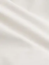 Pantalón cropped holgado color crema, confeccionado en sarga de algodón regenerativo. Presenta cintura plisada, cierre mediante botón y cremallera, bolsillos de hendidura y bolsillos traseros ribeteados.