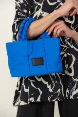 Cartera azul acolchada con asas trenzadas y parche rectangular negro.