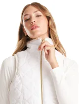 Chaleco reversible marca Weekend Routine, con un lado de piel sintética suave en tonos beige y blanco, y el otro lado capitoneado en blanco con diseño de rombos. Cuenta con cuello alto, bolsillos delanteros y cierre metálico dorado.